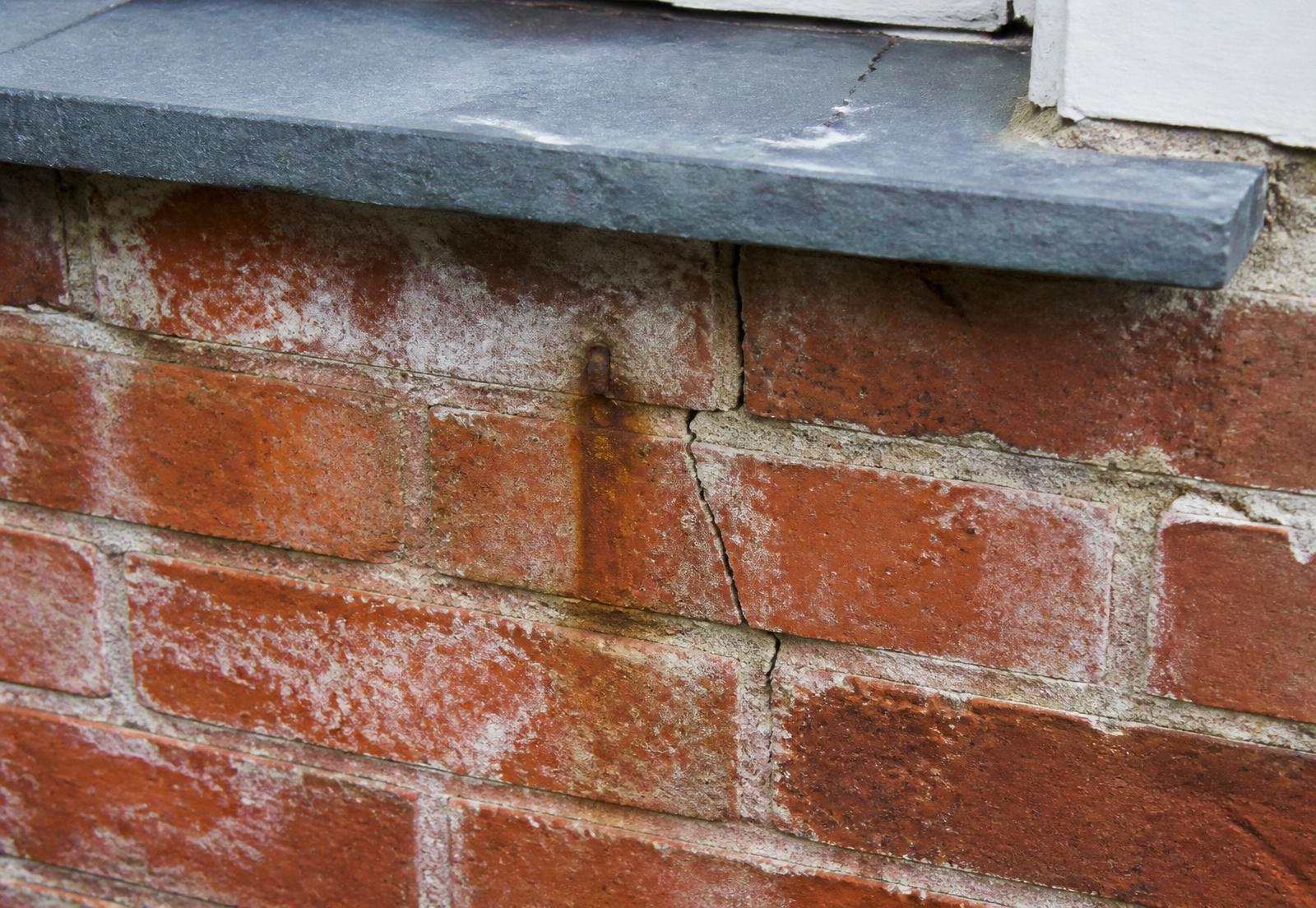 Close-up of Victorian brickwork showing a hairline crack, rusting wall tie stain and slate sill